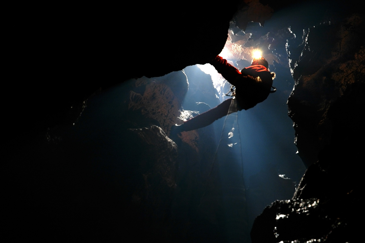 Caver using SRT equipment to descend into a deep cave